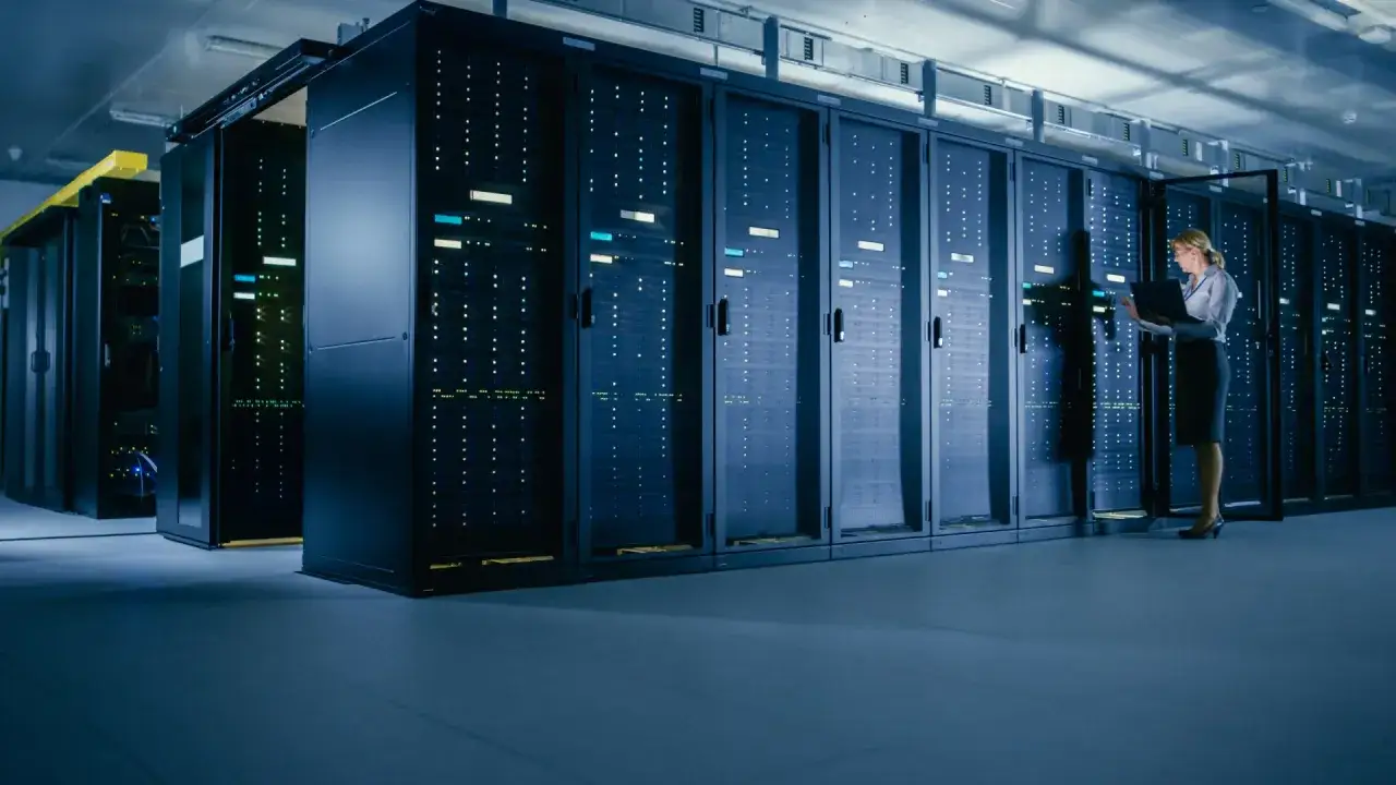 Kobieta z laptopem pracuje w serwerowni, gdzie rządzą potężne maszyny mainframe.