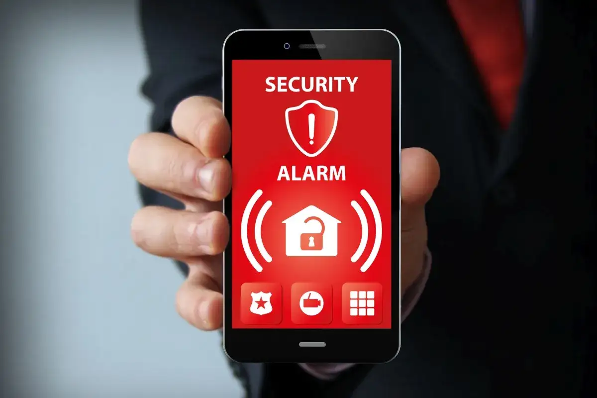 Telefon z ekranem pokazującym alarm bezpieczeństwa i ikonę domu z otwartą kłódką. To jak najlepszy antywirus na telefon, chroniący przed zagrożeniami.