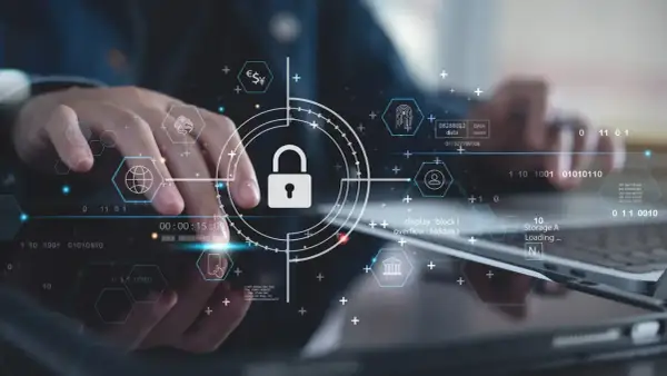 Ręce pracujące nad technologią, symbol kłódki i ikony sieciowe podkreślają znaczenie cyber security.