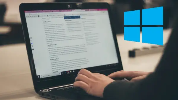 Osoba pisze na laptopie, na ekranie widać artykuł o malowaniu dachu. W tle widnieje niebieskie logo Windows.