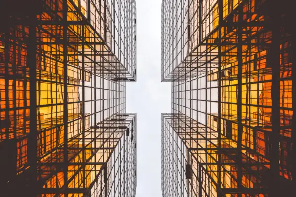 Szklane wieżowce odbijające pomarańczowe światło, tworzące geometryczny wzór. Czysta architektura w nowoczesnym wydaniu.