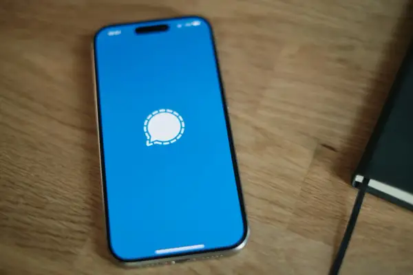 Telefon z niebieskim ekranem i ikoną komunikatora Signal. Obok leży czarny notatnik.