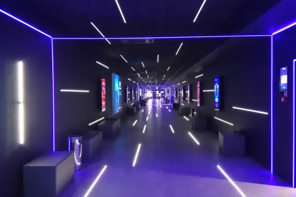 Nowoczesny korytarz multikina z neonowym oświetleniem, idealny do projekcji filmowych dzięki zaawansowanemu projektorowi laserowemu.